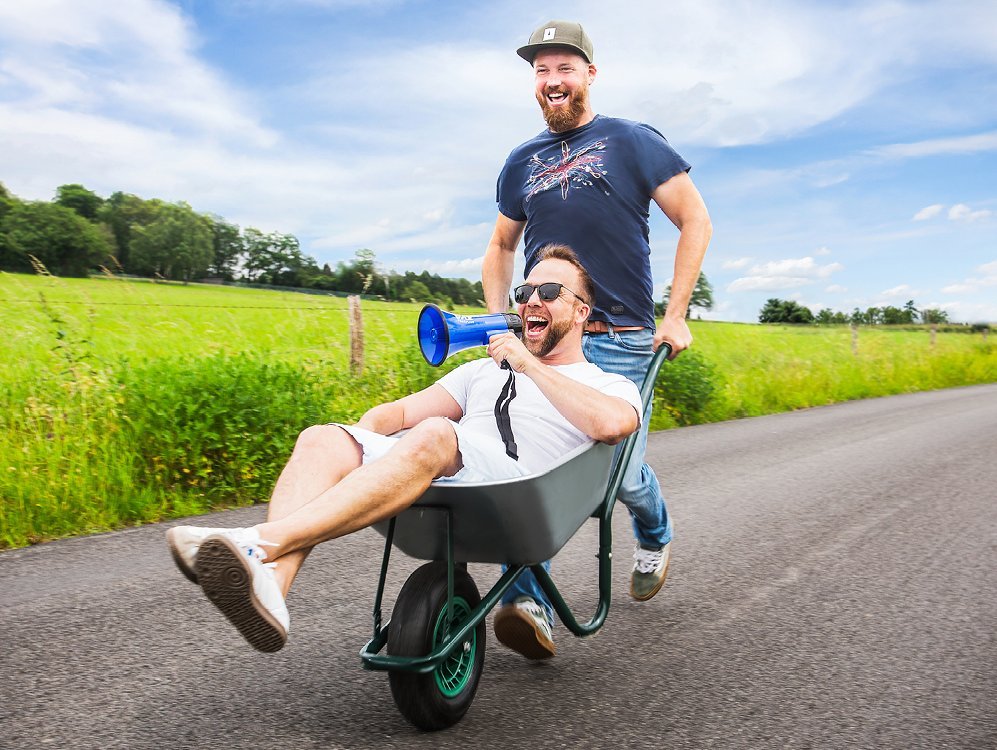 Ein Mann schiebt einen anderen Mann in einer Schubkarre