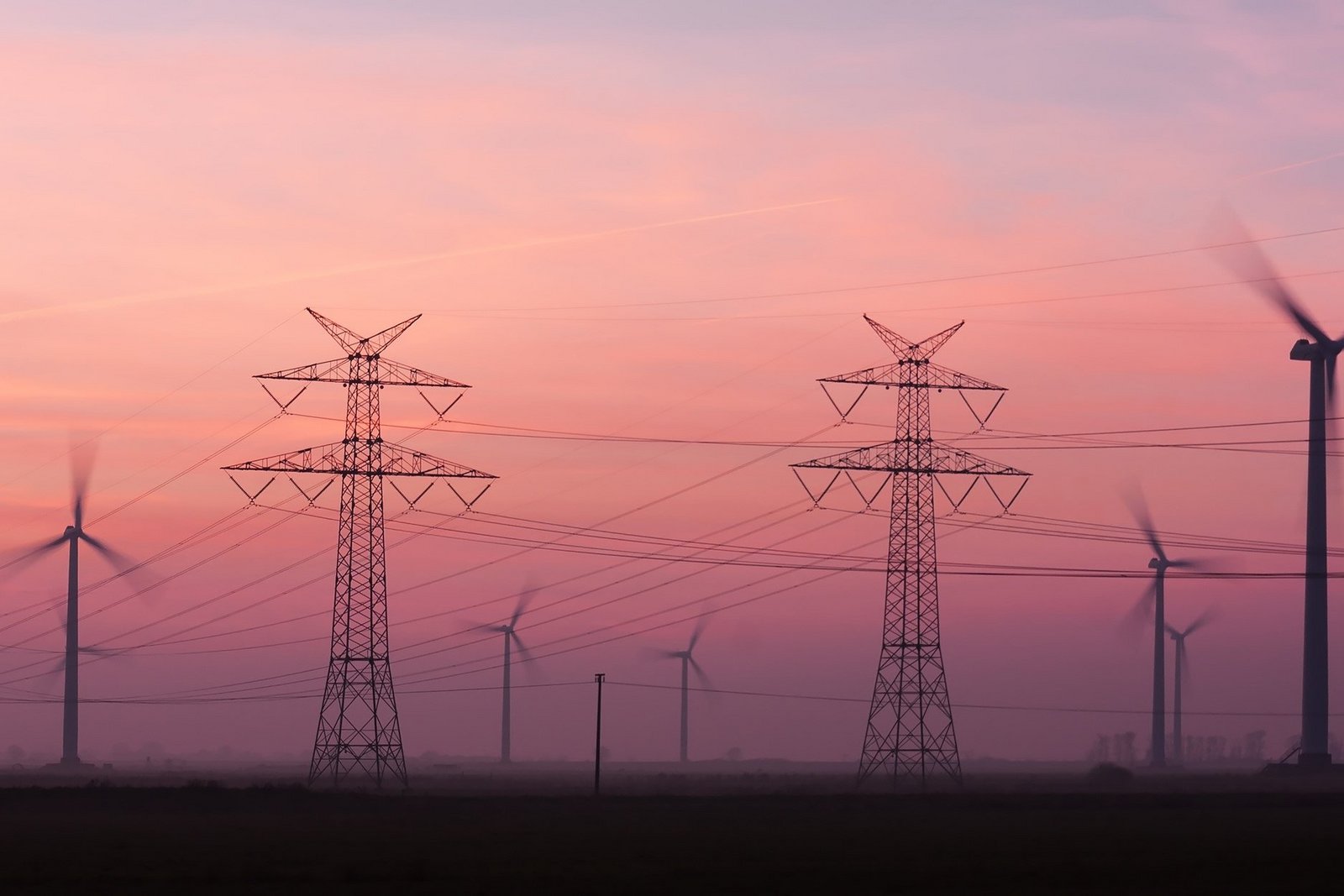 Strommasten und Windräder in einer Landschaft bei Sonnenuntergang.