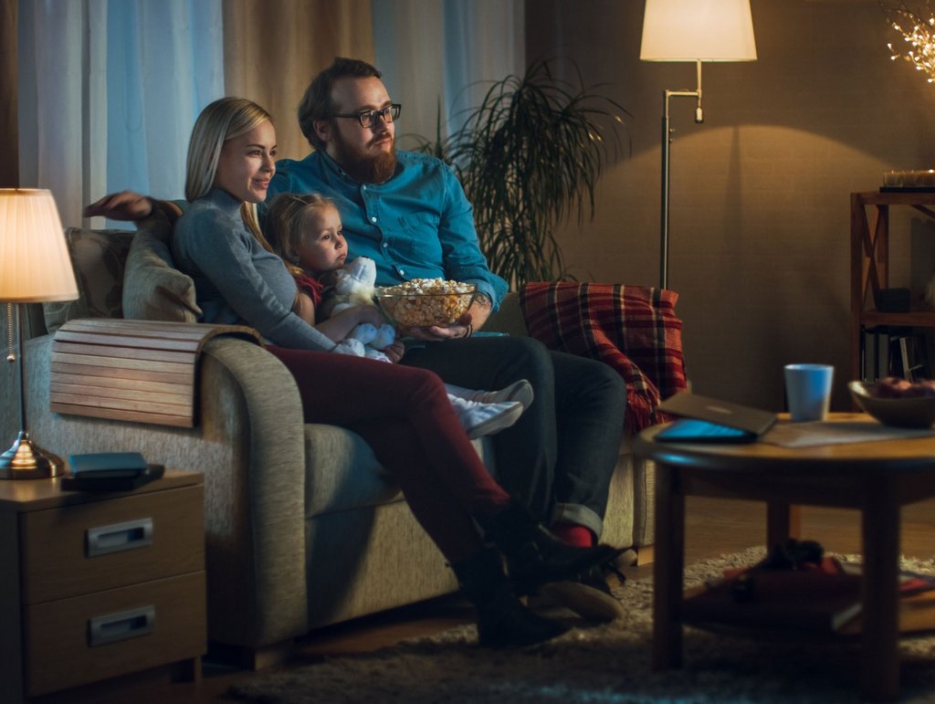 Familie mit kleiner Tochter guckt einen Film in beleuchtetem Zimmer