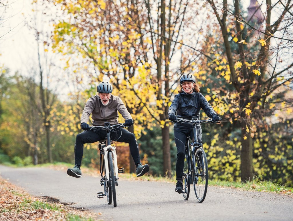 Ein älteres Ehepaar fährt mit E-Bikes auf einem Waldweg